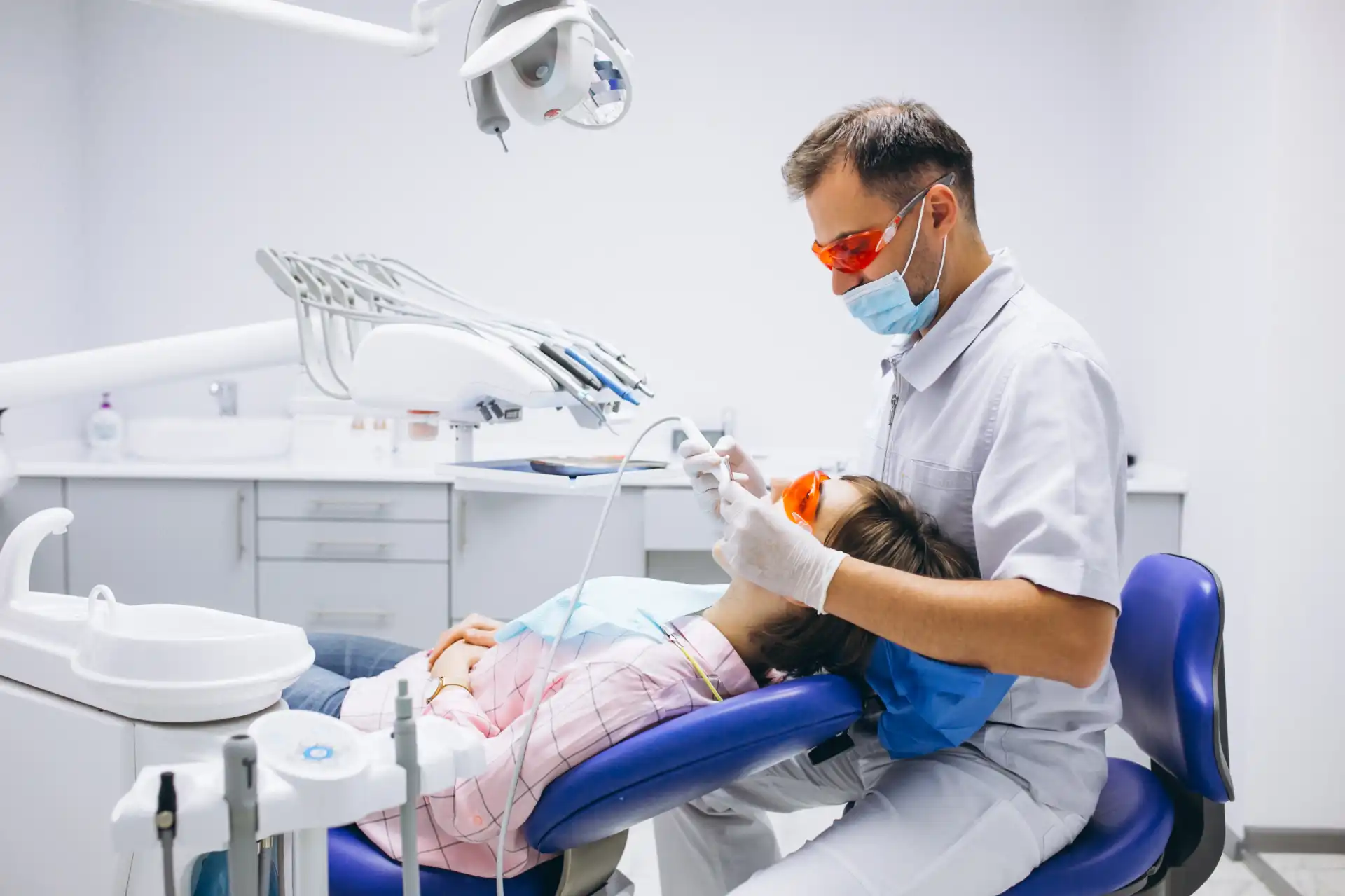 Dentista realizando tratamento odontológico em paciente na clínica, com equipamentos modernos e equipe de saúde bucal.